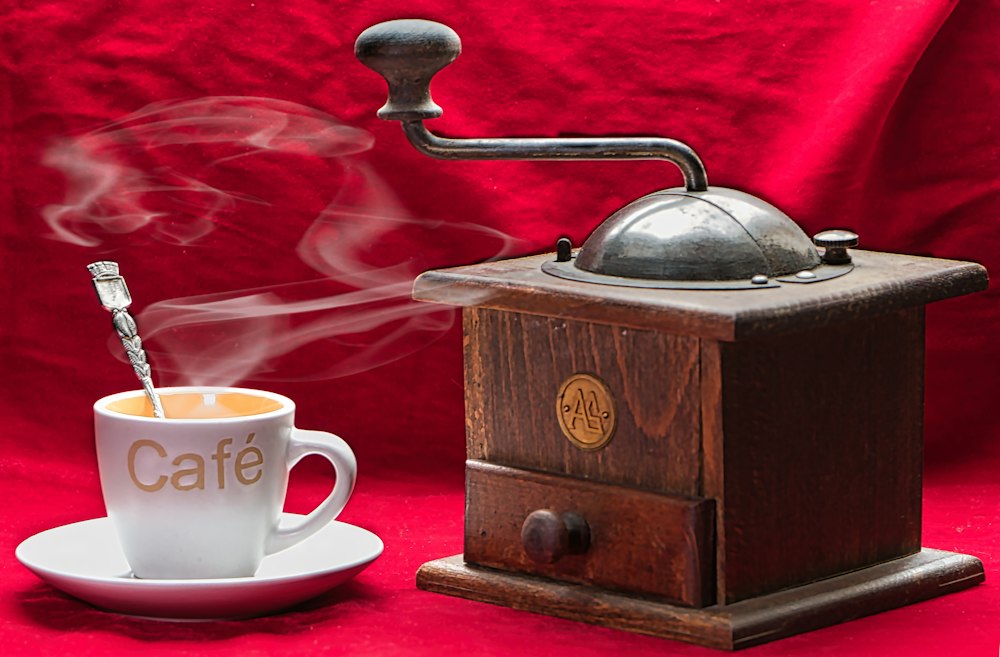 Molinillo manual de madera con una taza de café sobre fondo rojo